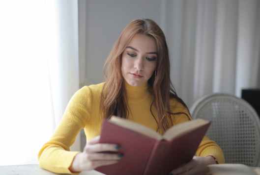 woman in yellow turtleneck sweater reading book